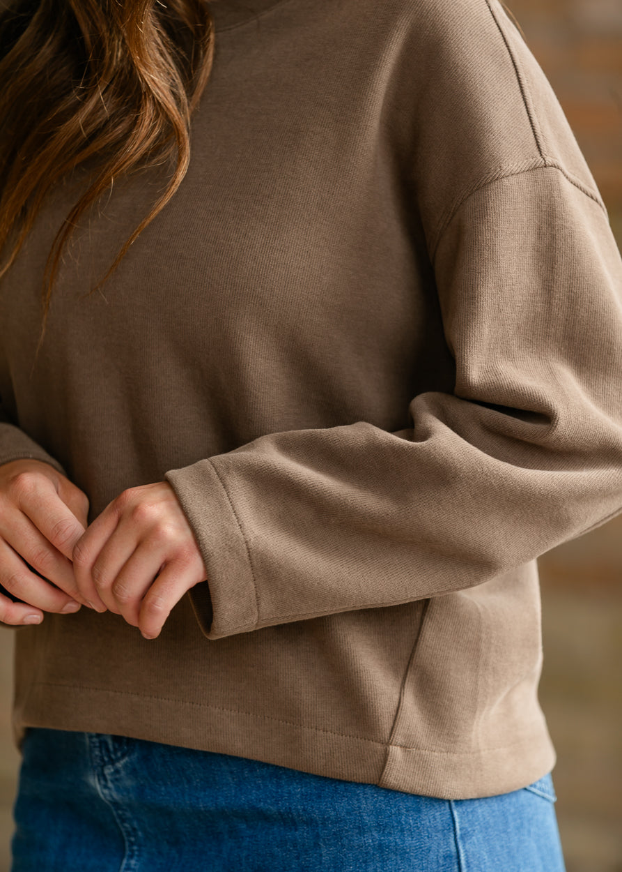 Close-up of brown round neck pullover sweater showing dropped shoulder construction and soft knit texture.