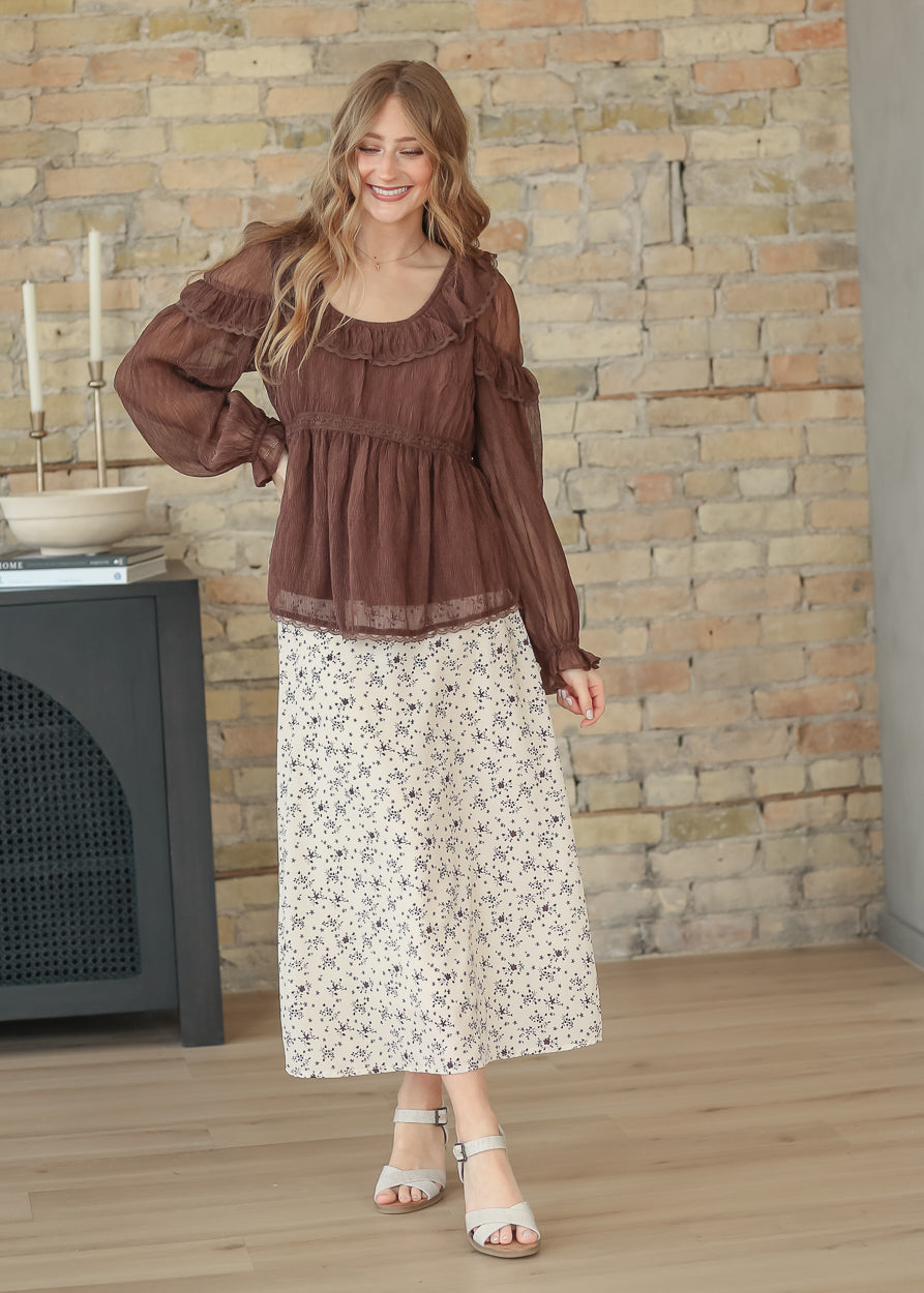 Brown ruffle long sleeve top styled with the Braylyn brown floral midi skirt and neutral sandals.