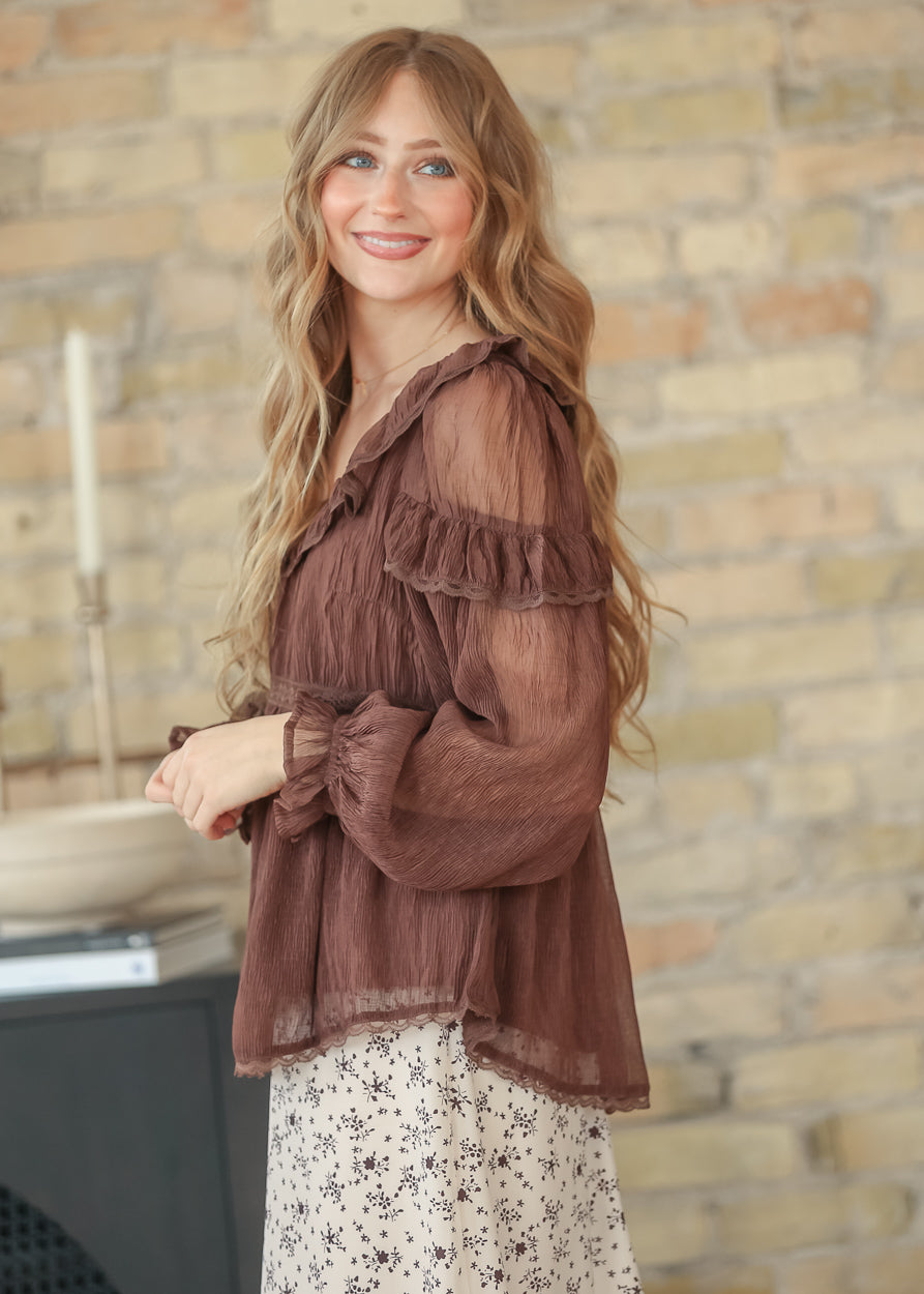 Side view of brown ruffle long sleeve top with balloon sleeves and empire waist, styled with a floral midi skirt.