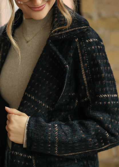 Close-up of black multi houndstooth coat showing soft texture, lapel collar, and warm neutral pattern.