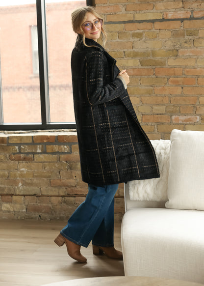 Side view of long black houndstooth coat with open front and knee-length hem, styled over denim.