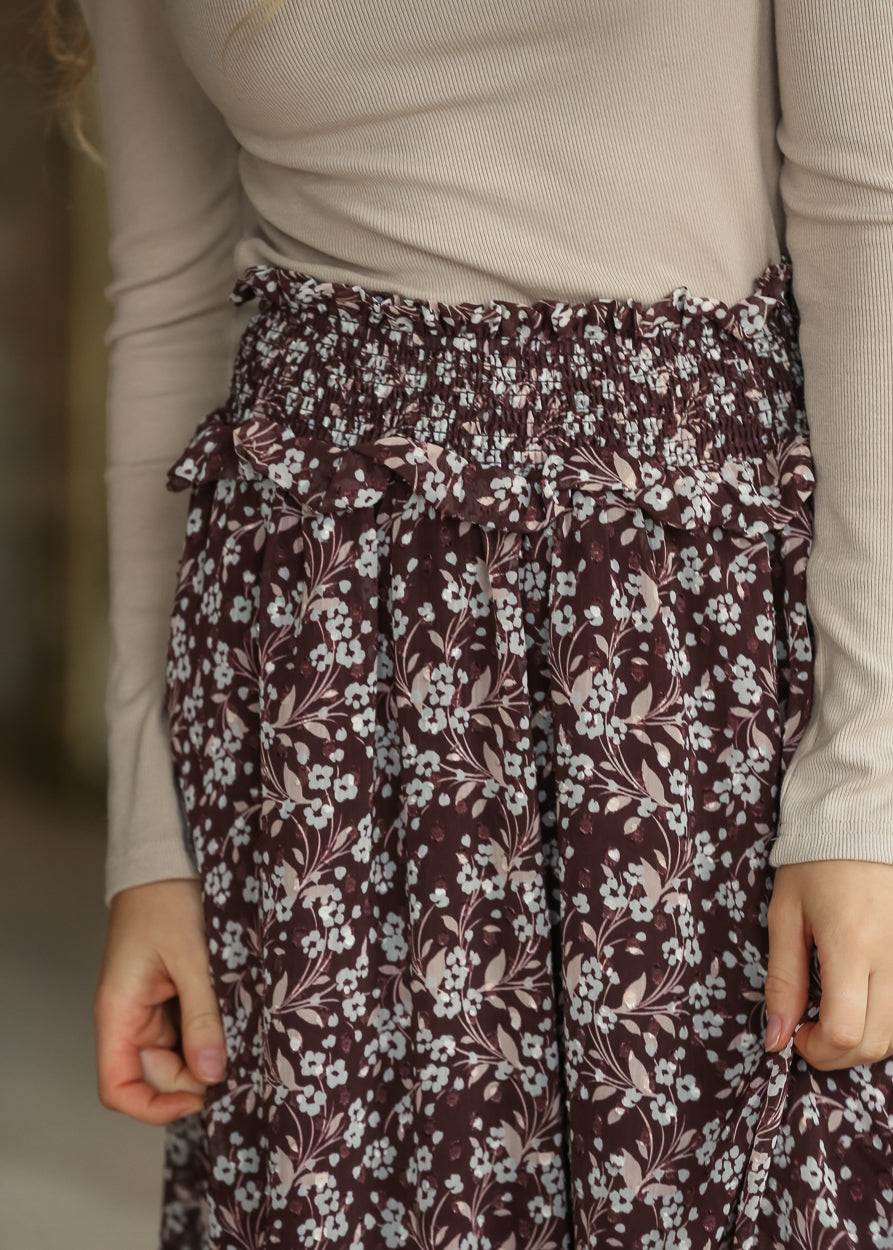 Close-up of brown floral midi skirt showing the wide shirred waistband and ruffle trim.