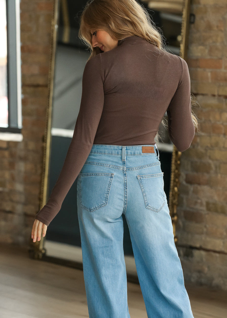 Back of fitted brown long-sleeve knit top styled with light wash denim.