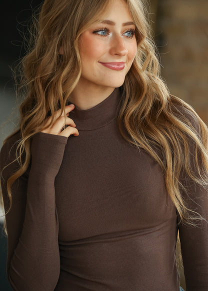 Brown ribbed mock neck top with long sleeves and thumbhole cuffs, styled with light wash wide leg jeans.