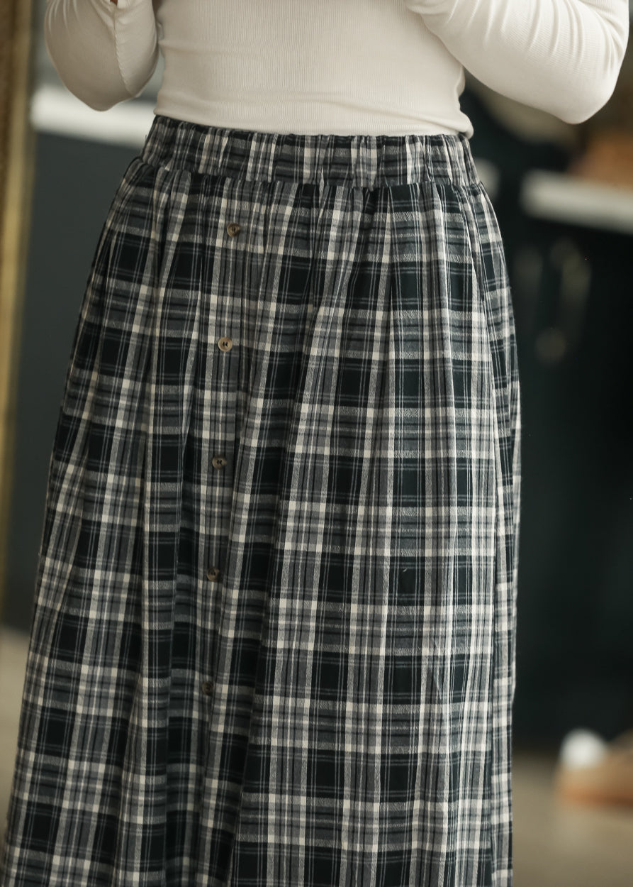 Close-up of black plaid midi skirt showing gathered waistband and button-front detail.