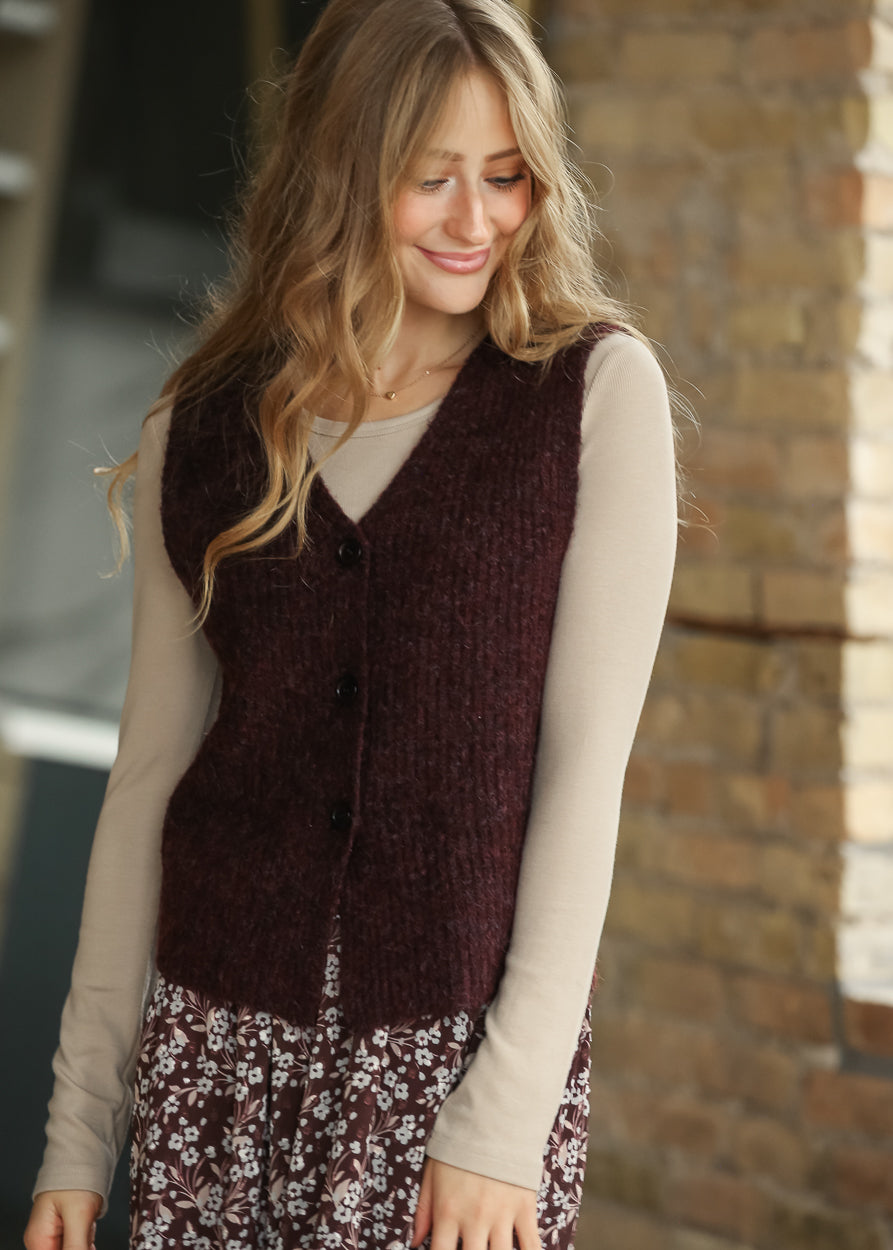 Close-up of burgundy sweater vest showing the V-neckline, fuzzy knit texture, and black buttons.