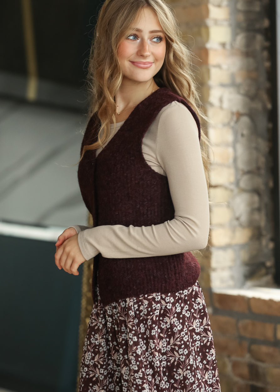 Side view of burgundy button-front sweater vest layered over a taupe long sleeve top.