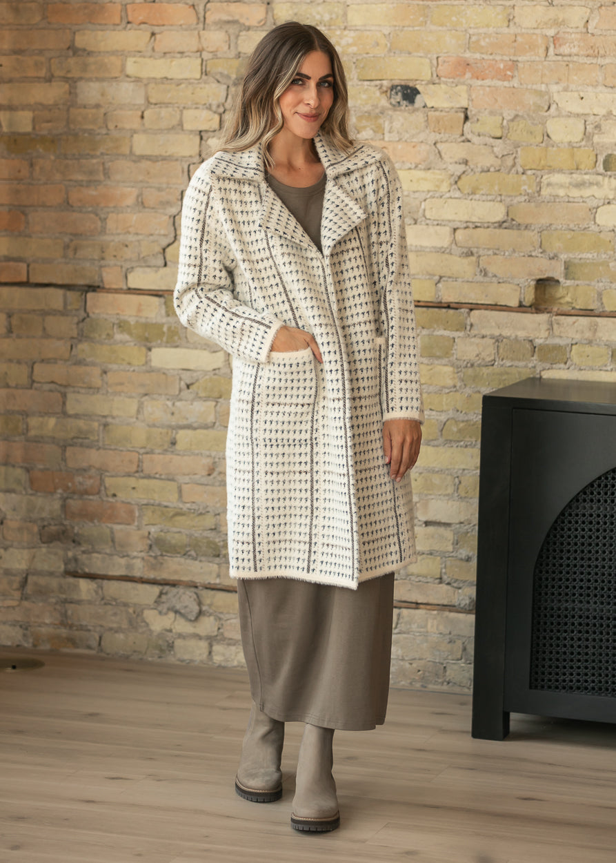 Cream houndstooth knee-length coat with patch pockets, styled over a taupe maxi dress with tall boots.