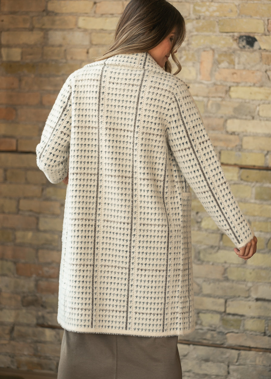 Back of the cream houndstooth coat showing knee-length hem and vertical contrast seam details.