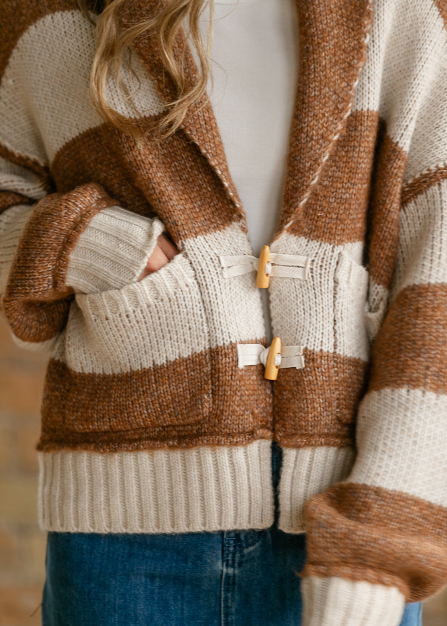 Close-up of chestnut striped sweater showing functional toggle closures and front patch pockets.