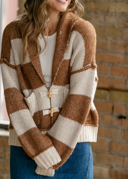 Close-up of chestnut striped sweater showing functional toggle closures and front patch pockets.