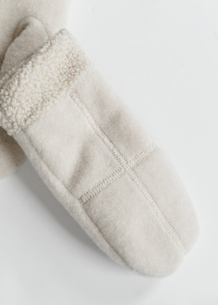 Ivory sherpa trim mittens styled with a black patterned coat and neutral knit top.