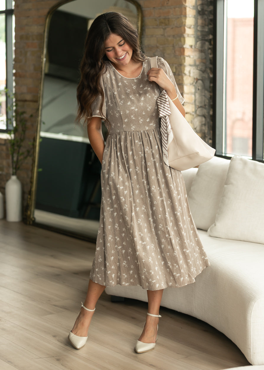 Brown floral midi dress with short flutter sleeves and ivory trim, styled with a cream tote and heels.