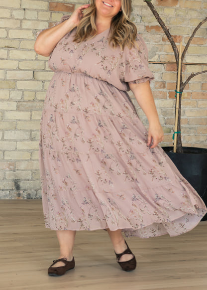 Floral maxi dress with V-neckline, short puff sleeves, elastic waist, and flowing tiered skirt, styled with brown flats.