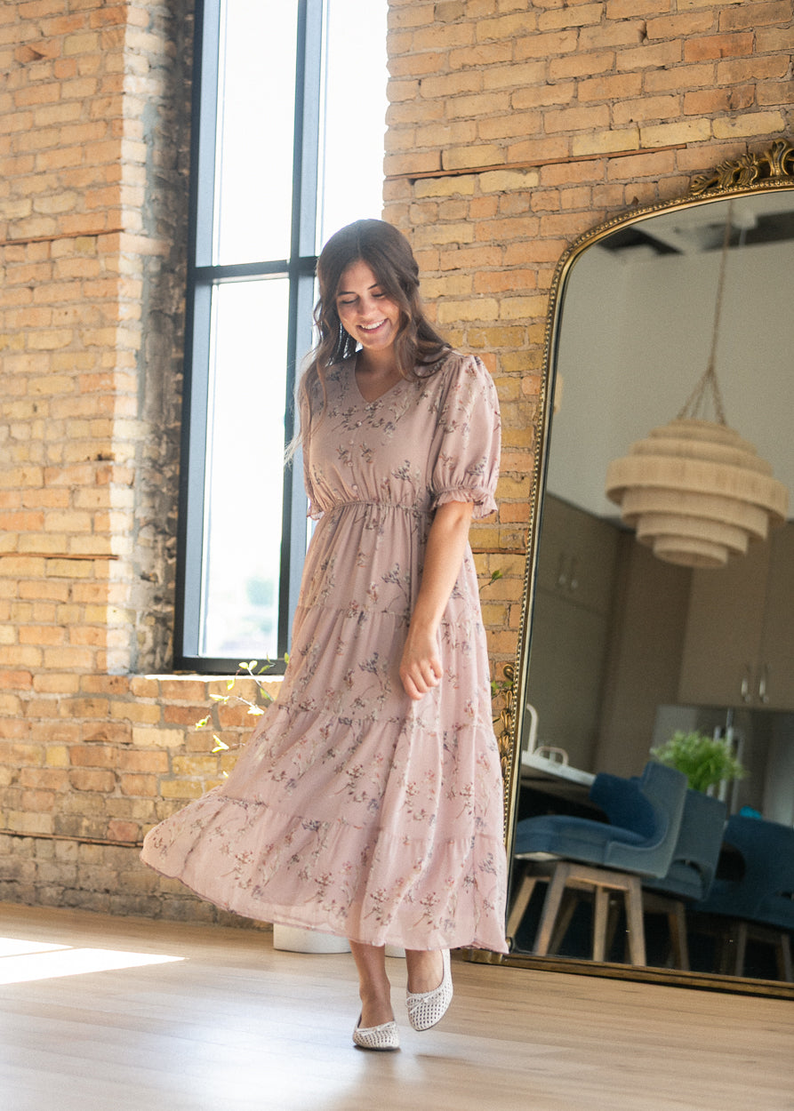 Blush pink floral V-neck maxi dress with a flowing tiered skirt, styled indoors with woven flats.