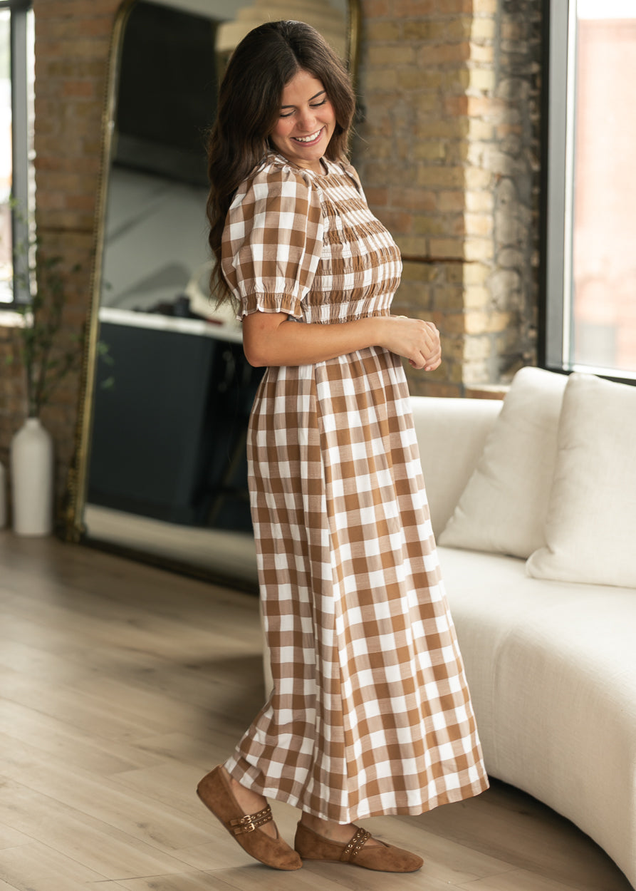 Brown plaid short sleeve midi dress in side view, showing the flowing lined skirt and smocked bodice.