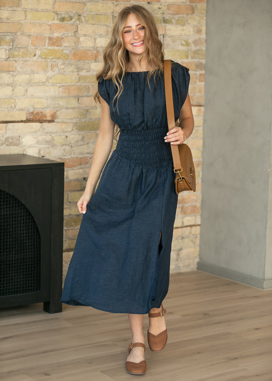 Dark wash sleeveless denim maxi dress styled with brown heels and a tan crossbody bag.