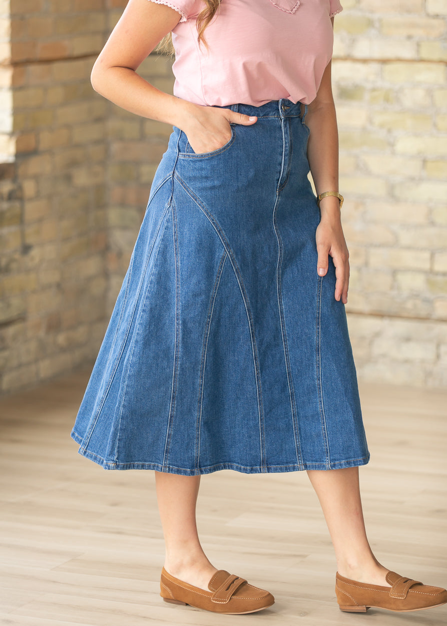 Close-up of medium wash denim midi skirt featuring curved stitch detailing and front pockets.