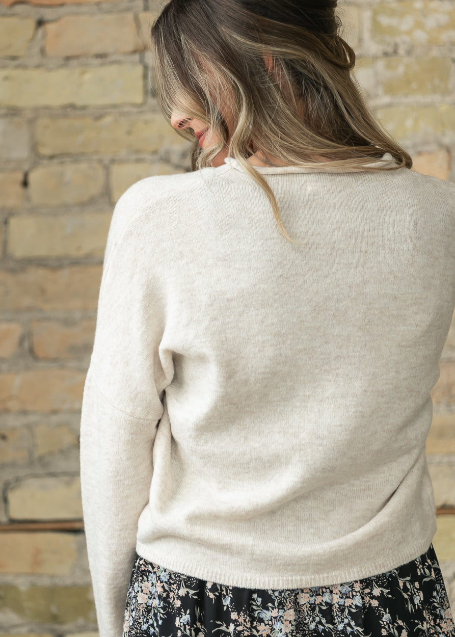 Close-up of heather beige cardigan knit texture and dolman sleeve, back view.