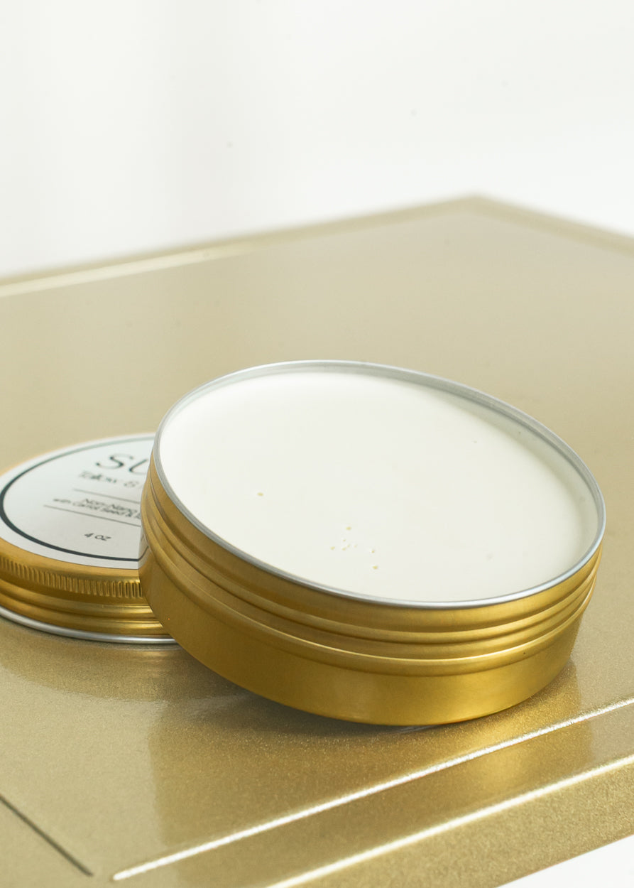 Open tin of mineral sun barrier balm showing smooth cream formula and gold container.