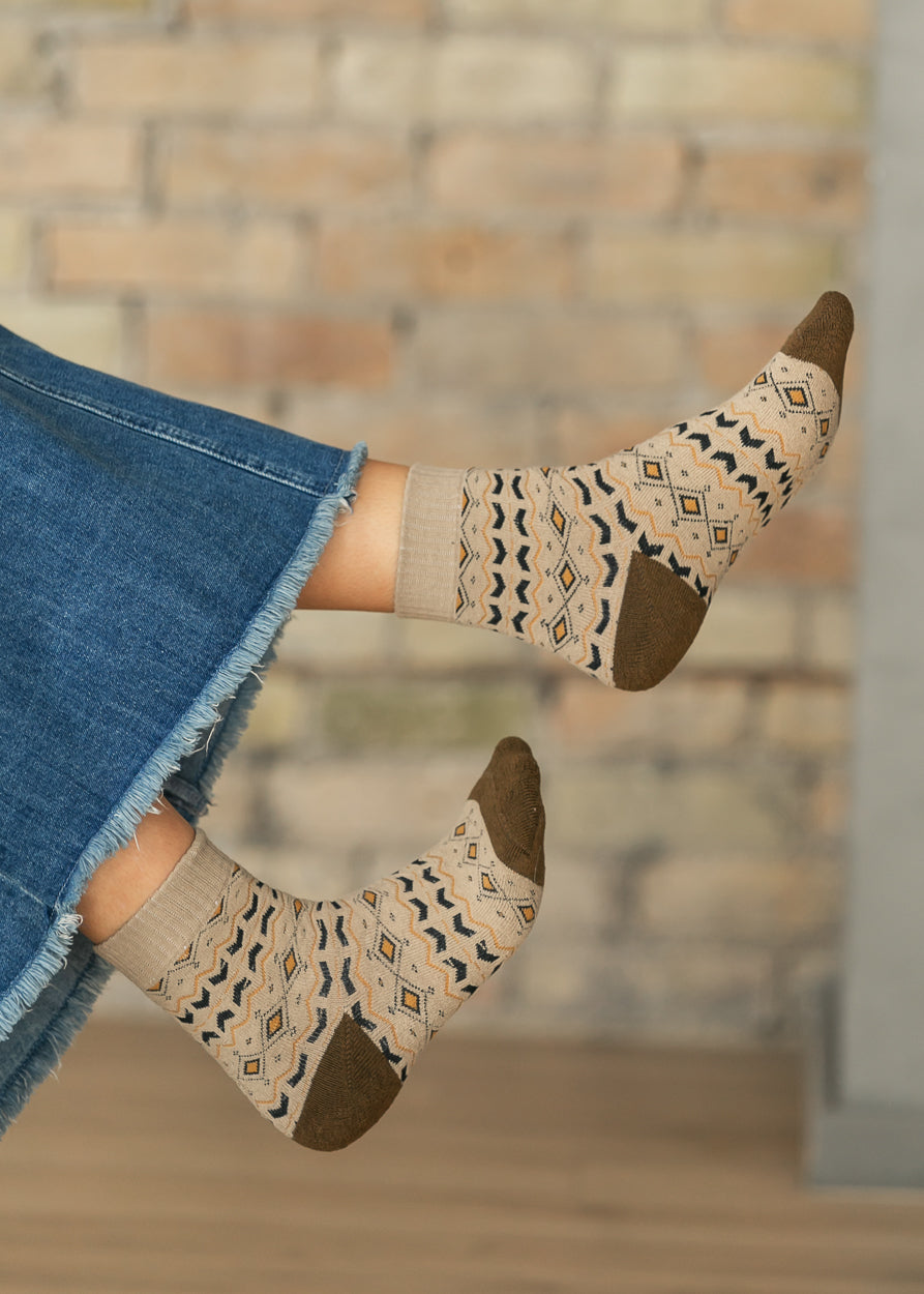 Tan Nordic Fair Isle crew socks with black and golden geometric pattern and brown heels, styled with a denim skirt.