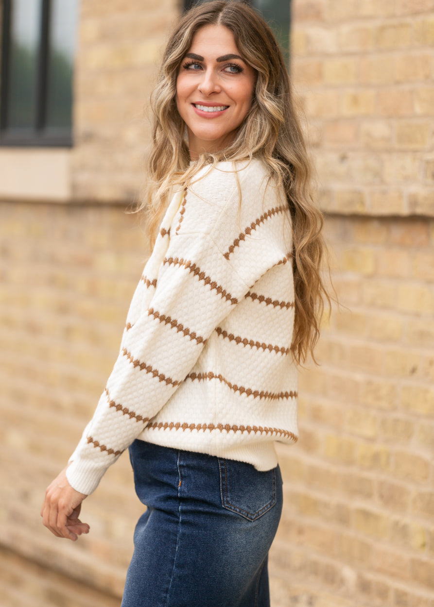 Cream and brown striped textured sweater with loose fit and long sleeves, styled with denim.