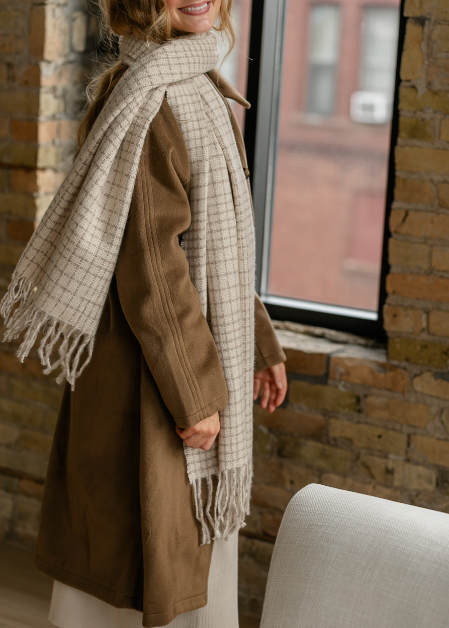 Ivory and taupe textured check scarf with fringe trim, draped over a brown button-front coat.