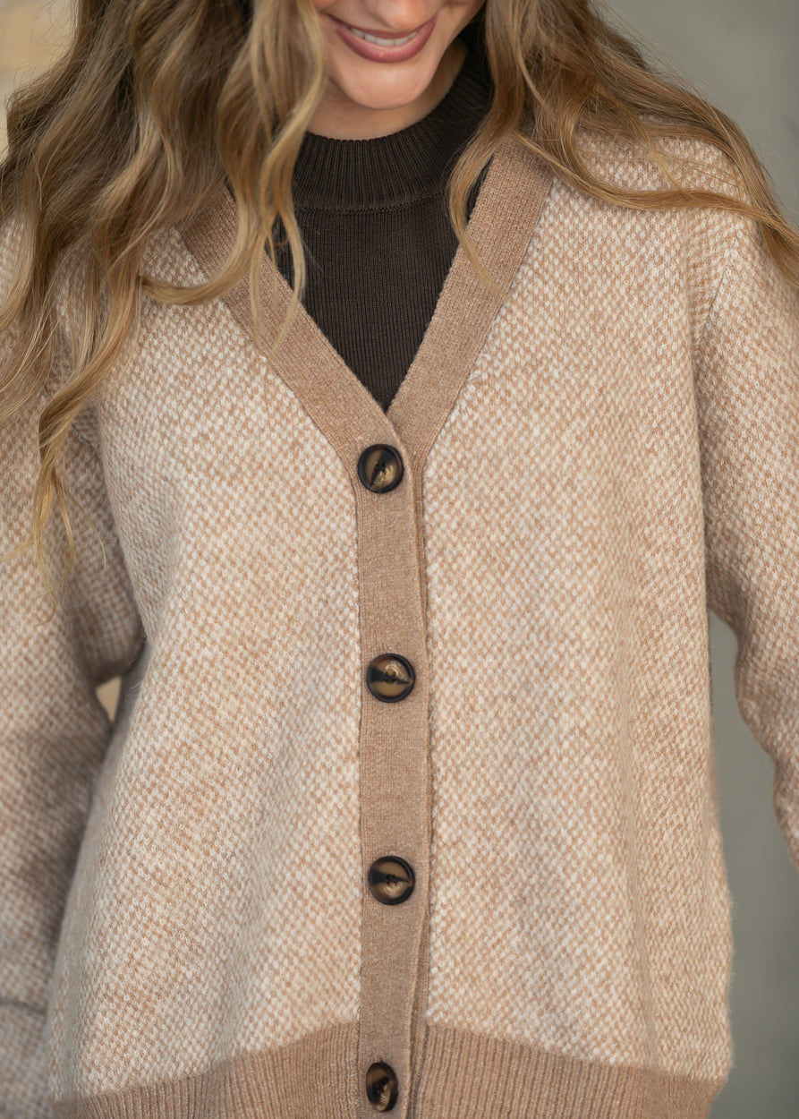 A close-up of a woman wearing a beige and tan textured knit cardigan with dark brown buttons over a dark brown turtleneck sweater.