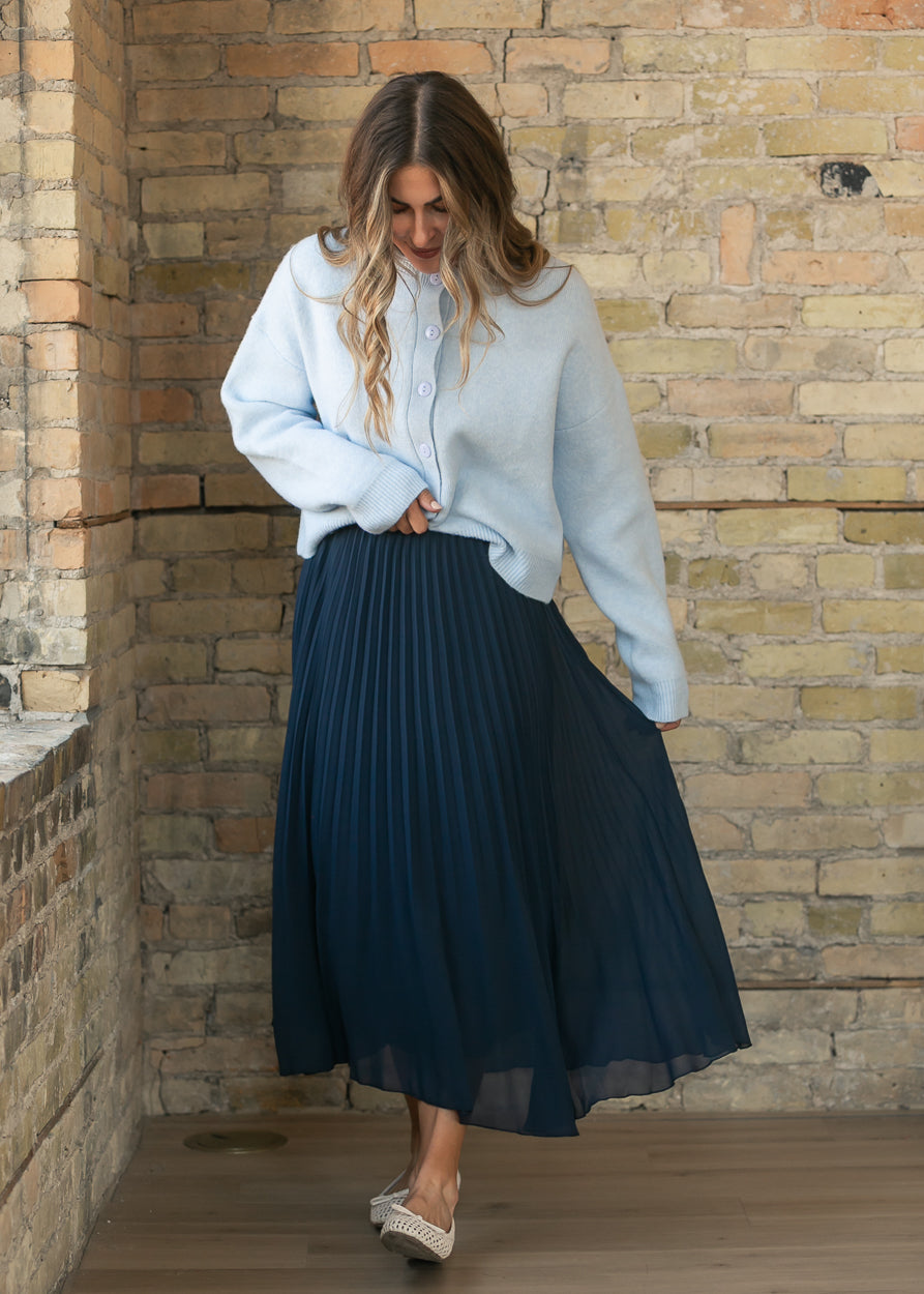 Navy flowy midi skirt with fine pleating and an elastic waist, styled with a button-front cardigan.