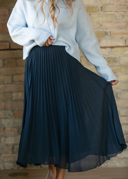 Navy pleated midi skirt with a flowy silhouette and elastic waist, styled with a light blue cardigan.