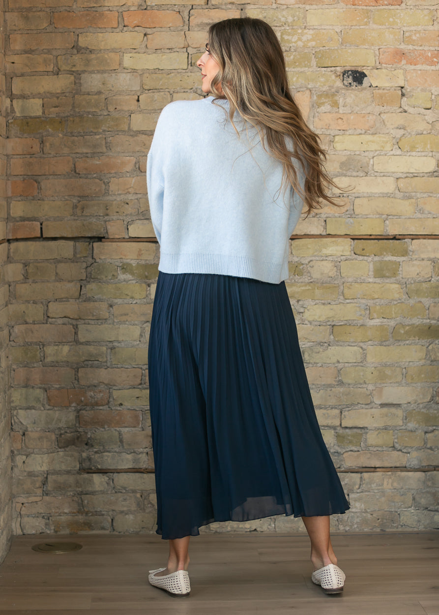 Back of navy pleated midi skirt showing the flowing mid-calf silhouette and fine pleating.