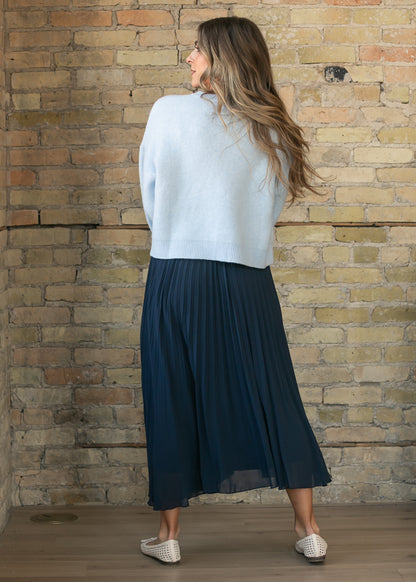 Back of navy pleated midi skirt showing the flowing mid-calf silhouette and fine pleating.