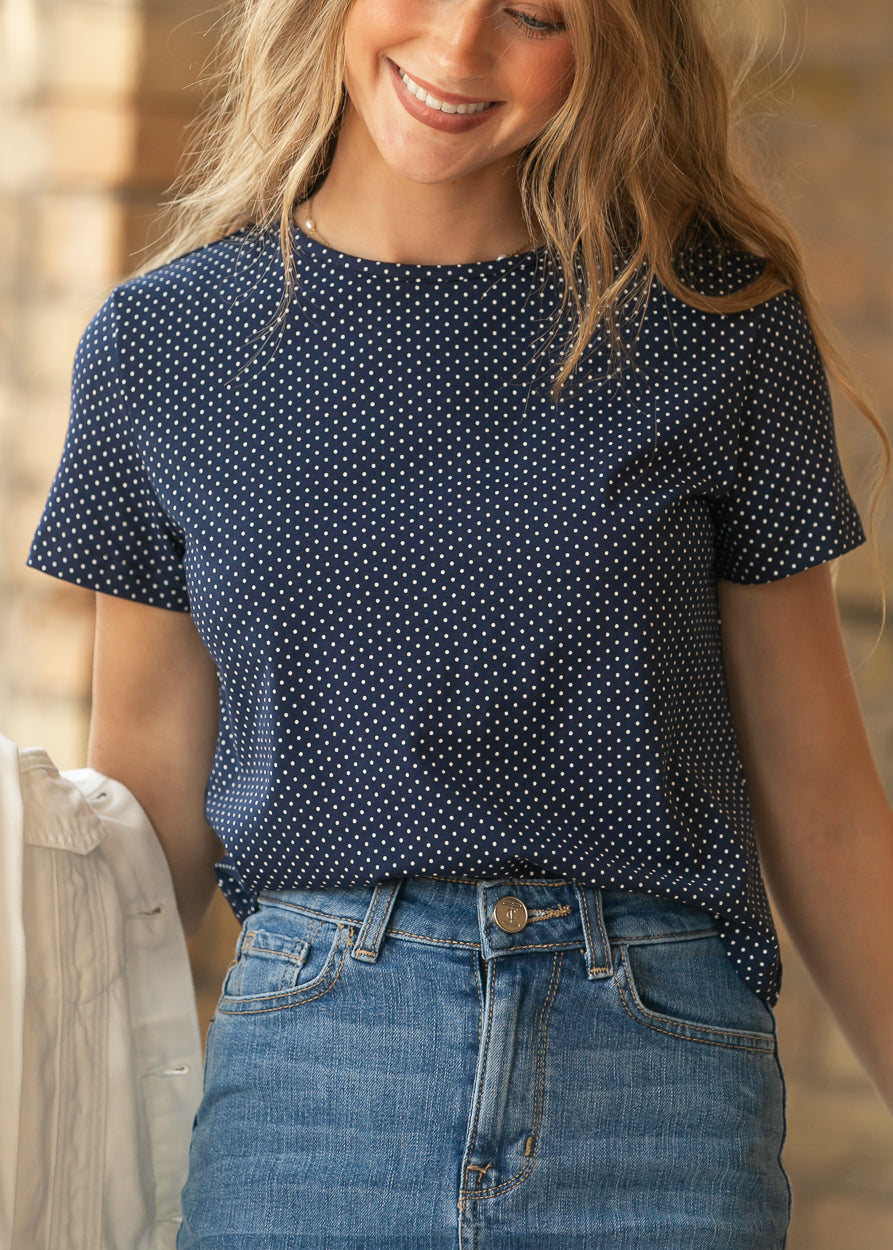 Close-up of navy polka dot jersey tee with crew neckline and short sleeves, styled with a medium wash denim skirt.