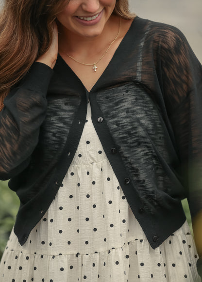Lightweight black cardigan styled over a cream tiered polka dot dress in natural light