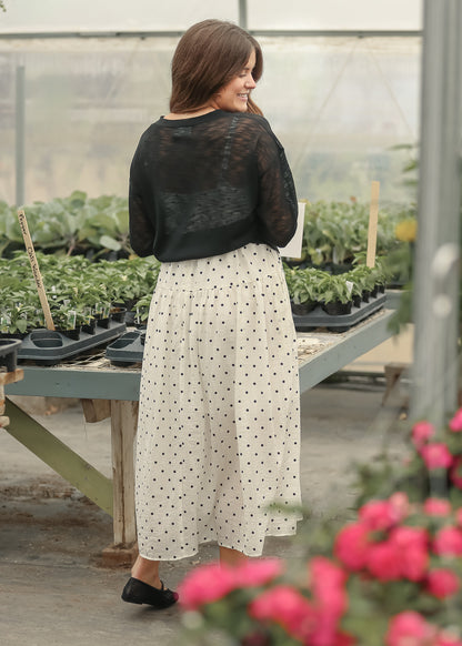 Black lightweight v neck cardigan layered over a cream polka dot maxi dress in a greenhouse