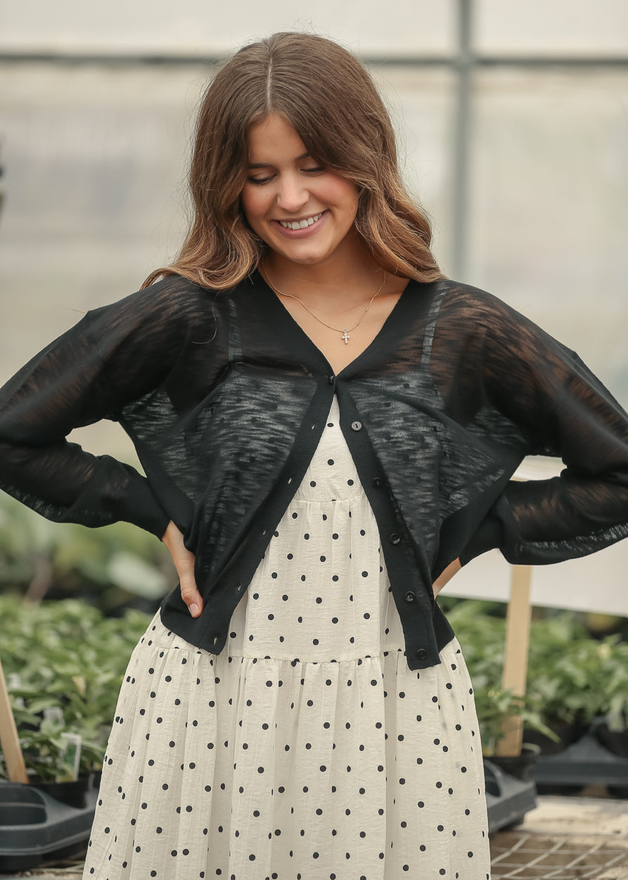Sheer black lightweight cardigan with button front and long sleeves styled over a tiered dress