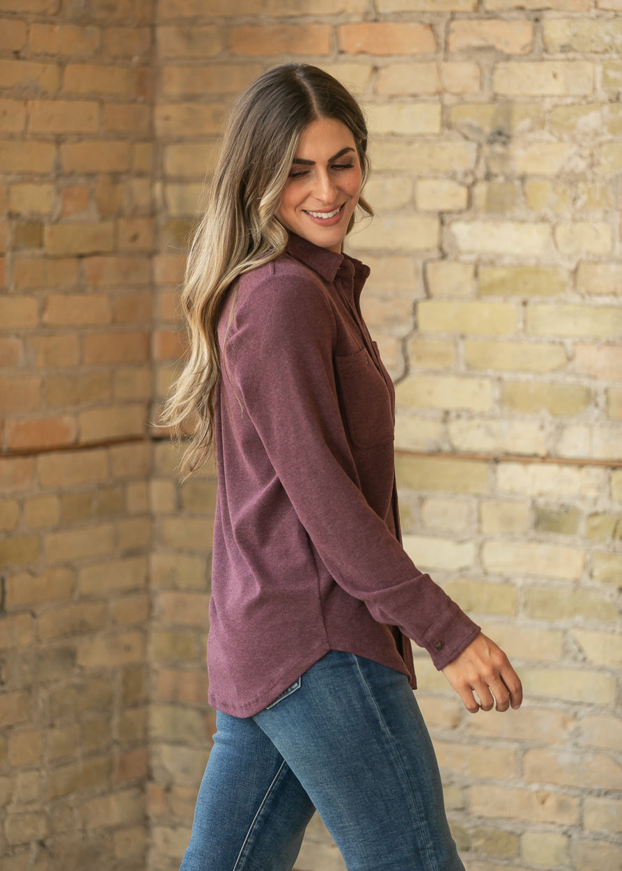 Side view of burgundy long sleeve button up top showing the relaxed fit and curved hem.