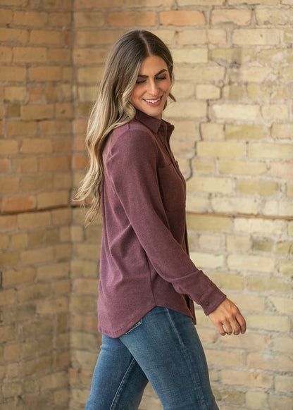 Side view of burgundy long sleeve button up top showing the relaxed fit and curved hem.