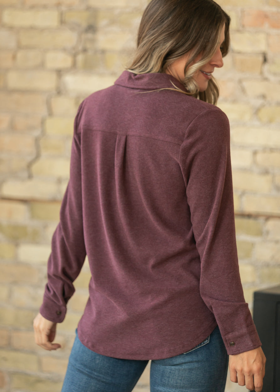 Back of burgundy button up top showing the back yoke, center pleat, and curved hip-length hem.