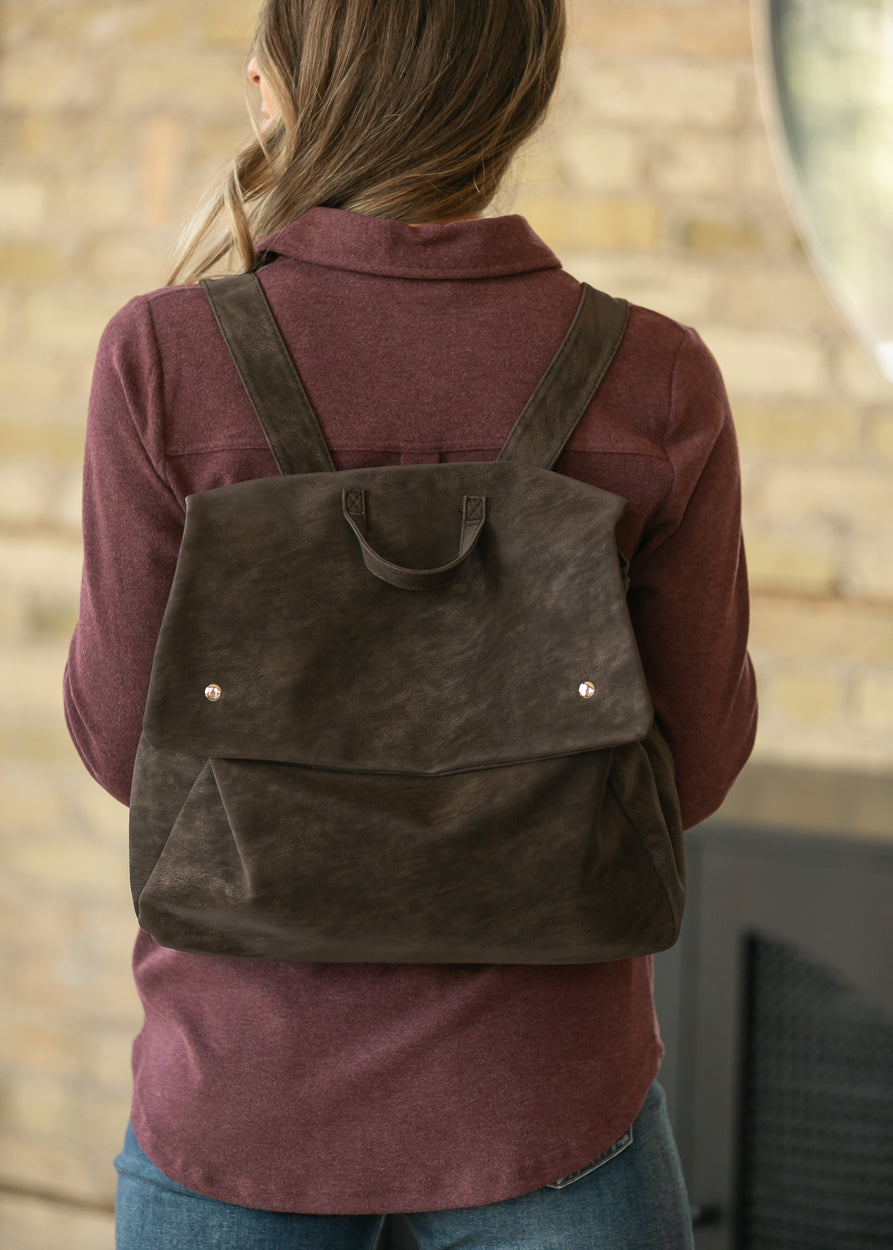 Back view of vintage chocolate brown backpack showing wide adjustable straps, fold-over flap, and relaxed shape.