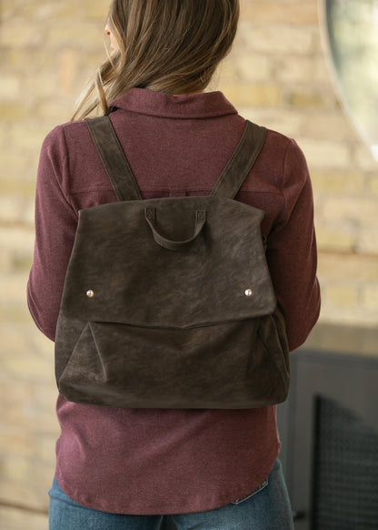 Back view of vintage chocolate brown backpack showing wide adjustable straps, fold-over flap, and relaxed shape.