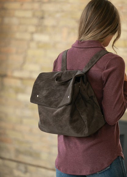 Angled view of chocolate brown matte backpack showing the fold-over flap, side profile, and shoulder straps.