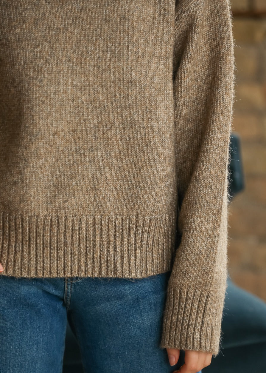 Close-up of sandstone heathered knit sweater showing ribbed hem and long sleeve cuff.