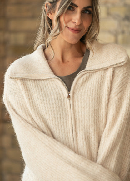 Close-up of Sterling oatmeal knit jacket showing ribbed texture, long sleeves, and zip collar.