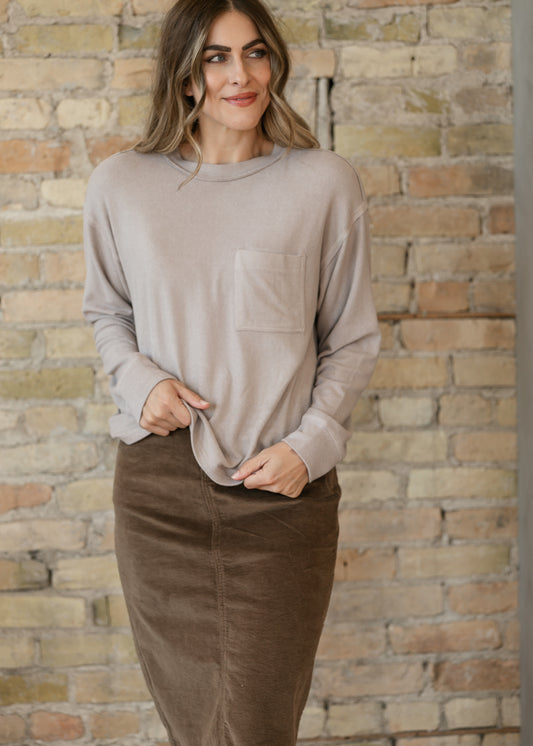 Heather taupe Sutter Pocket Front Top showing its loose silhouette and long sleeves, paired with a corduroy skirt.