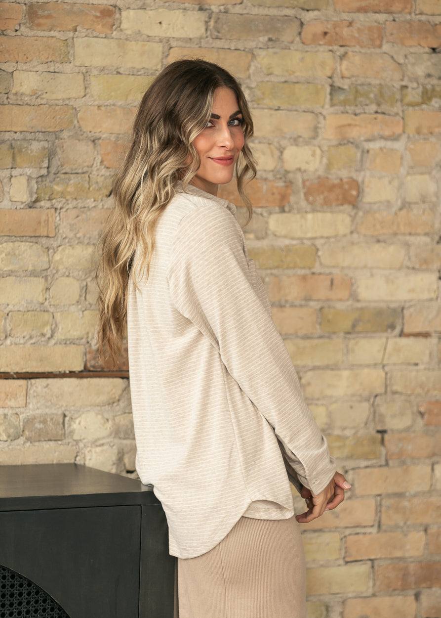 Side view of tan striped shirt showing relaxed drape and curved hem, worn open over a tan knit skirt.