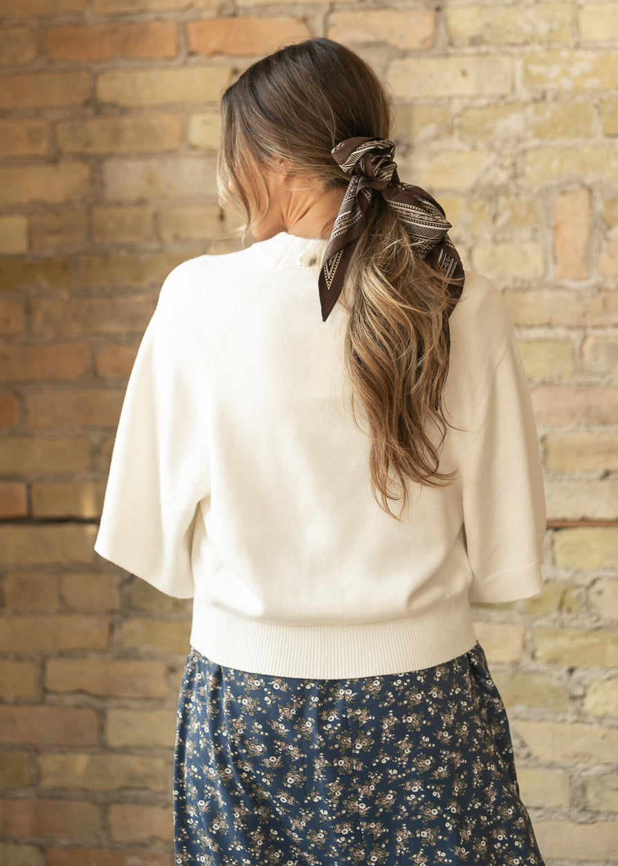Back of cream knit cardigan showing the loose fit, wide sleeves, and ribbed hip-length hem.