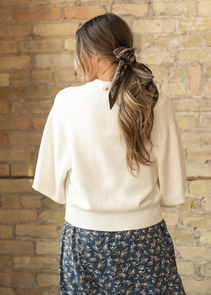 Back of cream knit cardigan showing the loose fit, wide sleeves, and ribbed hip-length hem.