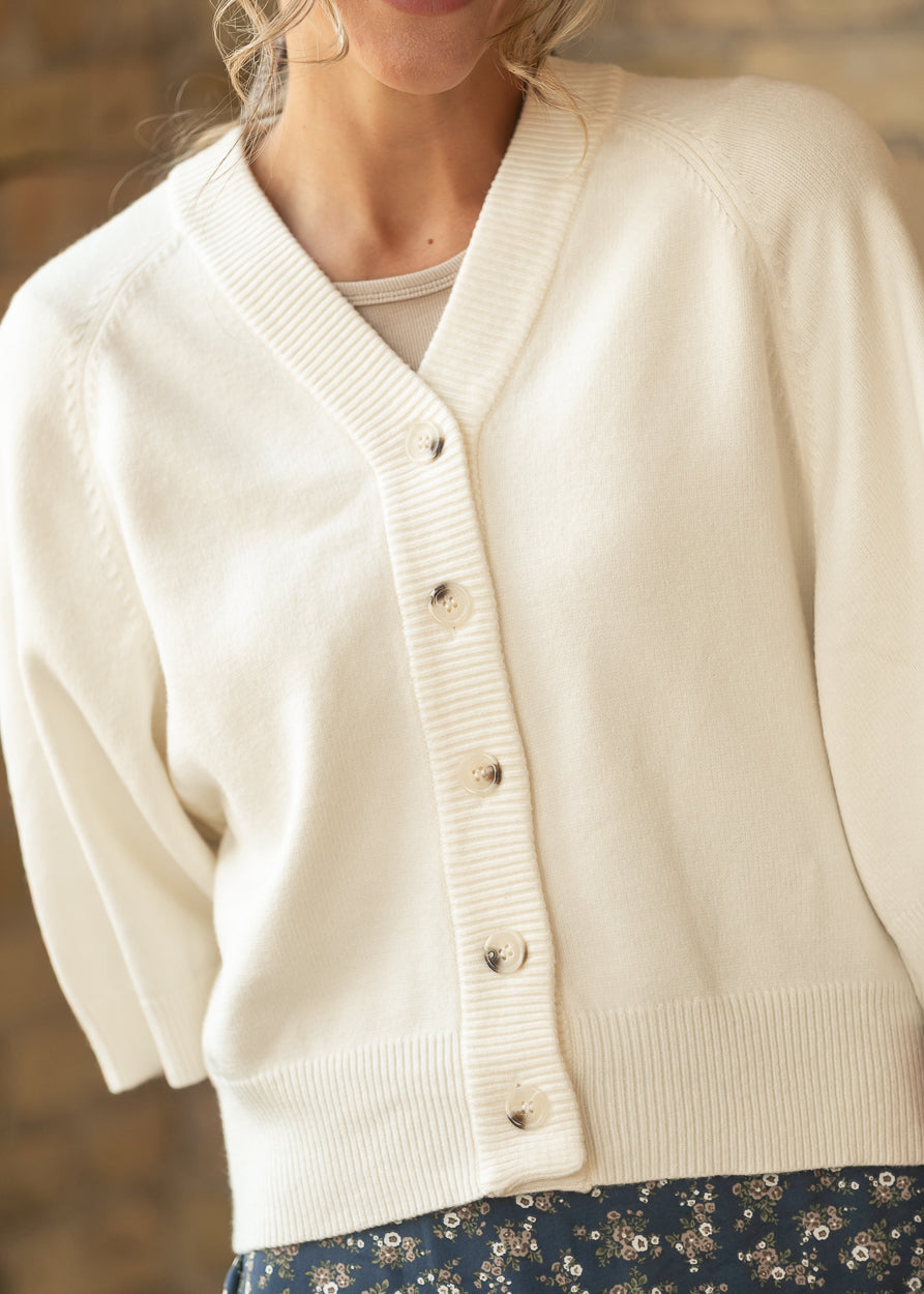 Close-up of cream knit cardigan showing the V neckline, button front, and ribbed trim.