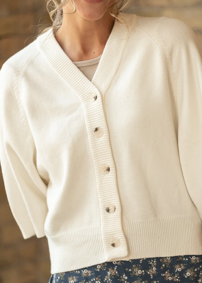 Close-up of cream knit cardigan showing the V neckline, button front, and ribbed trim.